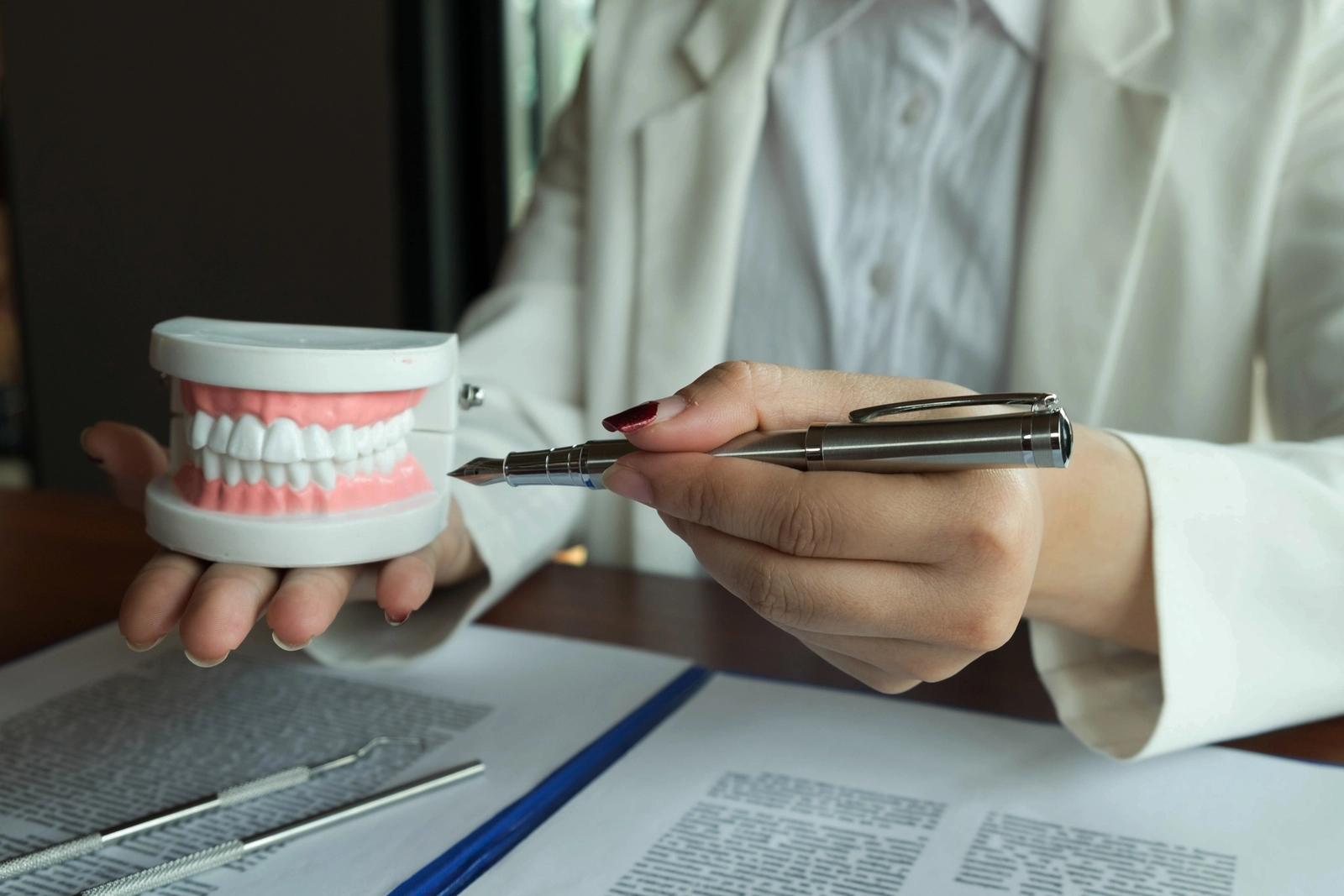 Orthodontist Schooling Requirements: A hand holding a mouth model and pointing at it with the other hand. On the table in front of them are several papers with a lot of text.