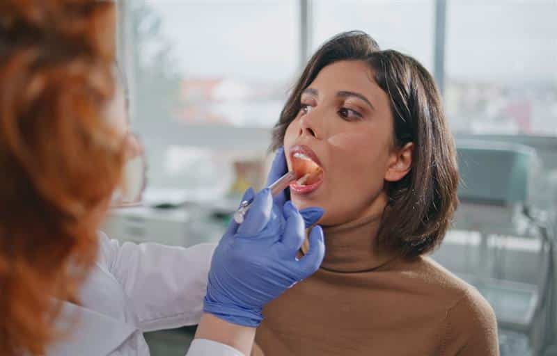 What Can Your Tongue Say About Your Health: A woman with her mouth open to allow a medical professional to examine her tongue